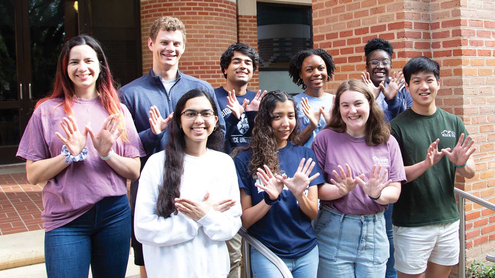 Group of Rice students holding up their hands in the owl signal