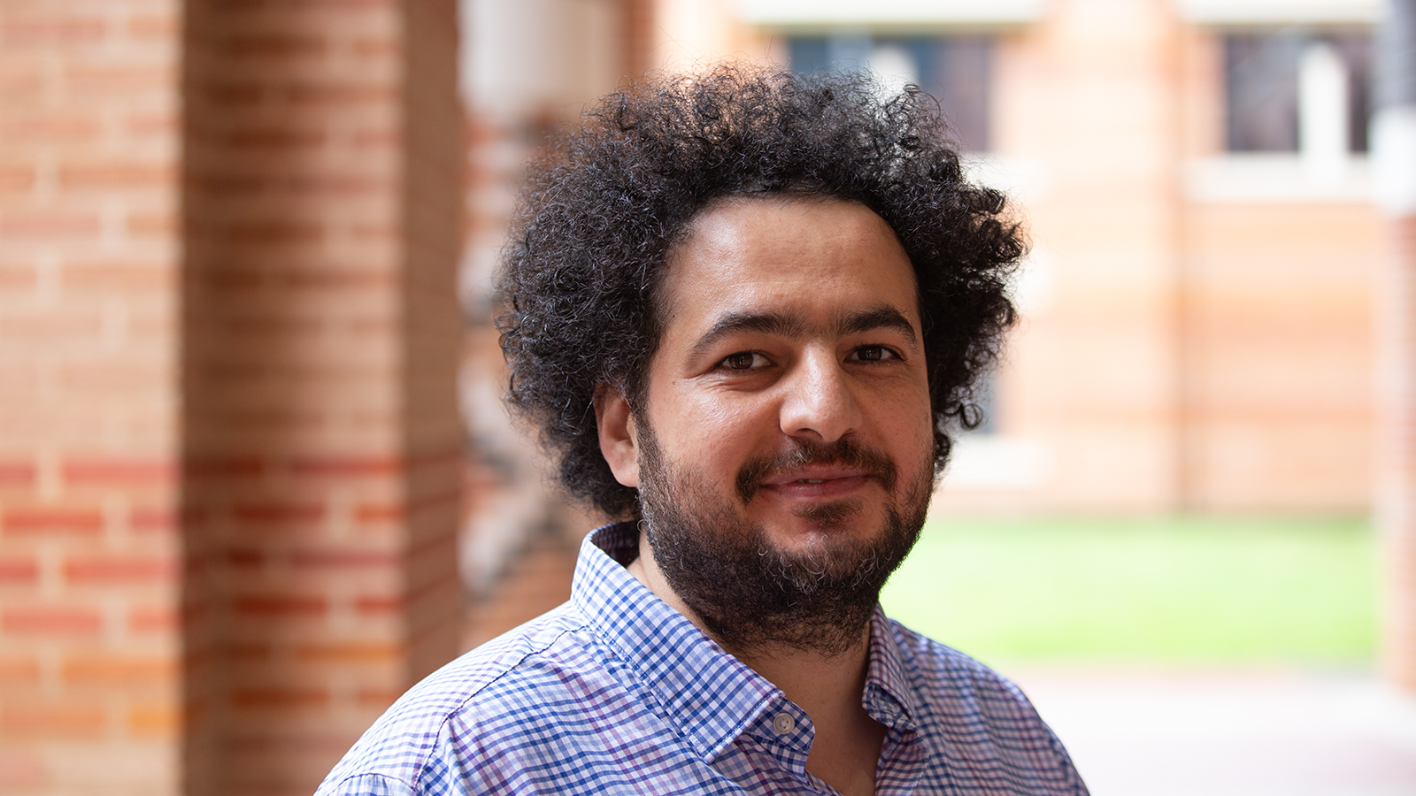 Professional headshot of Dr. Ali Siahkoohi in a blue plaid button-down shirt in front of brick background on Rice University campus.