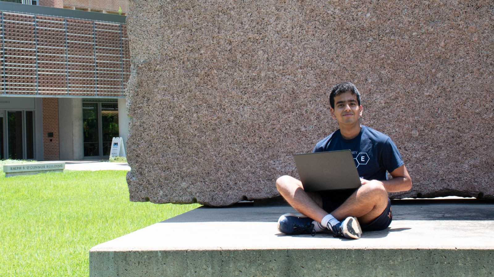 Rishi Madhuvairy sits with laptop in front of the O'Connor building