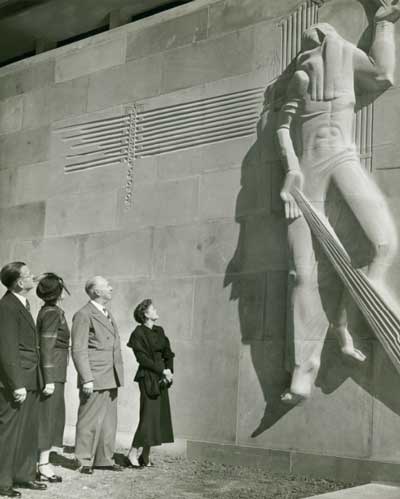 A view of the façade of the William M. Rice Institute’s Abercrombie Engineering Laboratory, shortly after its opening. A group including Texas oilman and philanthropist J.S. Abercrombie, his wife Lillie Frank, and daughter Josephine E. Abercrombie, along with an unidentified man are admiring the work of sculptor William McVey, showing an airborne figure with stylized rays emanating from its hand.