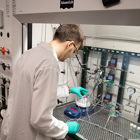 An individual in a white lab coat works with a reactor.